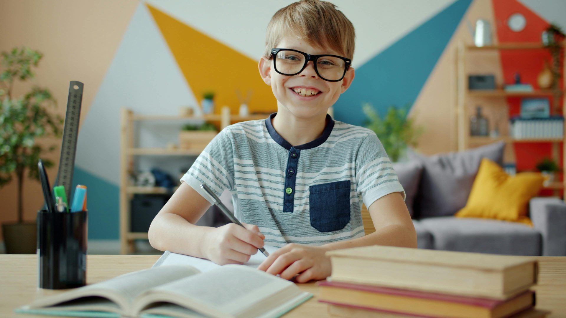 Un enfant joyeux portant des lunettes étudie à la maison. Un arrière-plan vif et coloré enrichit l'environnement d'apprentissage.