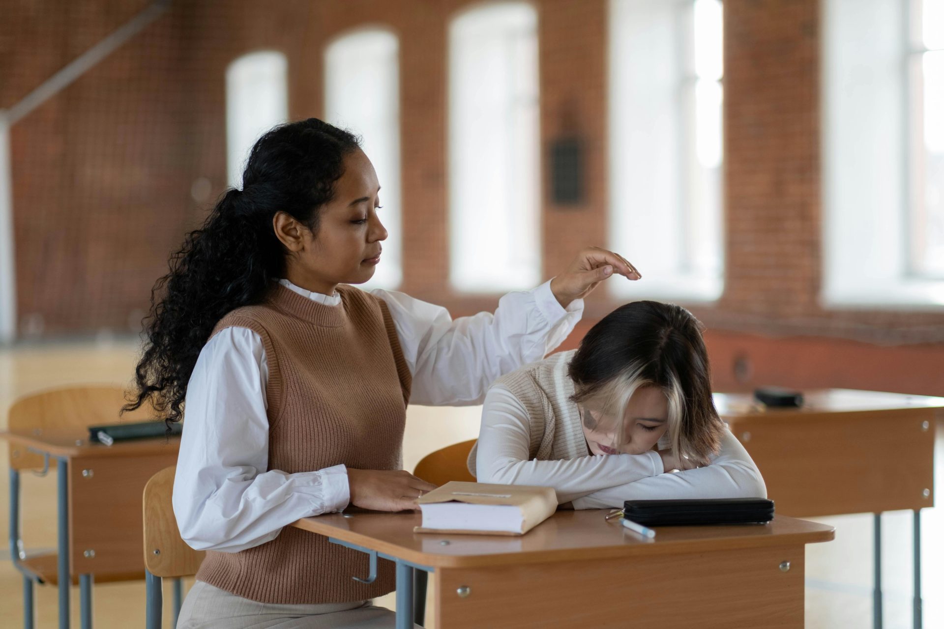 Zwei Frauen in einem Klassenzimmer, die an einem Schreibtisch Unterstützung und Trost spenden.